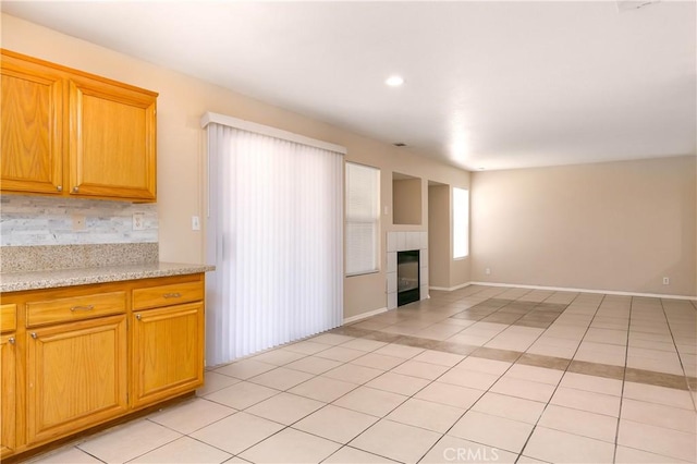 kitchen featuring a tiled fireplace, decorative backsplash, light tile patterned floors, and light stone counters