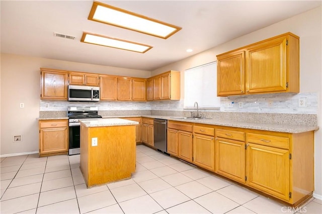 kitchen featuring sink, a center island, decorative backsplash, light tile patterned floors, and appliances with stainless steel finishes