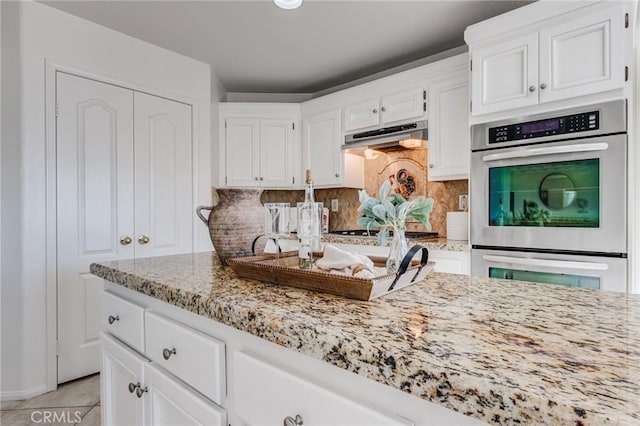 kitchen with light stone counters, under cabinet range hood, white cabinetry, appliances with stainless steel finishes, and backsplash