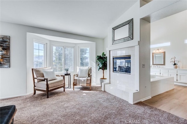 sitting room featuring baseboards, high vaulted ceiling, a tile fireplace, and light colored carpet