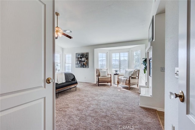 living area featuring baseboards, a ceiling fan, and light colored carpet