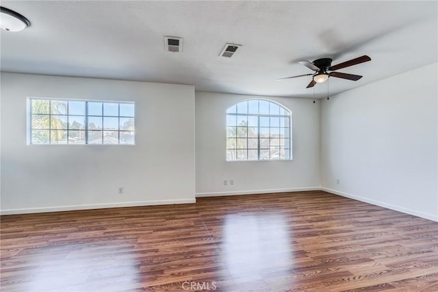 unfurnished room with a ceiling fan, visible vents, dark wood finished floors, and baseboards