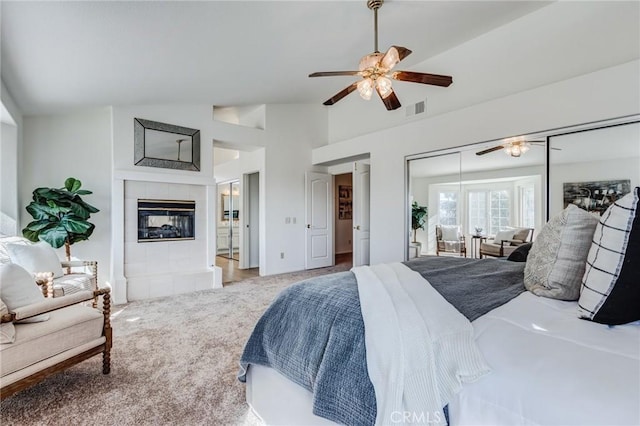 bedroom featuring visible vents, a ceiling fan, a tile fireplace, lofted ceiling, and light colored carpet