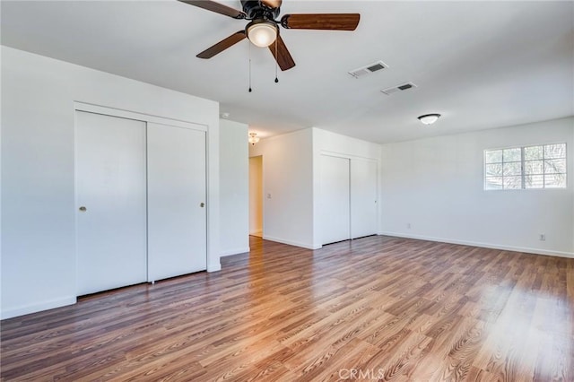 unfurnished bedroom featuring baseboards, visible vents, multiple closets, and wood finished floors