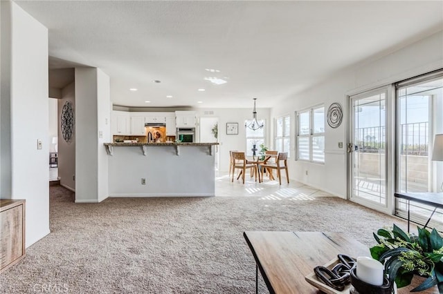 unfurnished living room featuring recessed lighting, light colored carpet, a notable chandelier, and baseboards