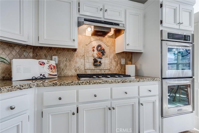 kitchen featuring under cabinet range hood, appliances with stainless steel finishes, white cabinetry, and decorative backsplash