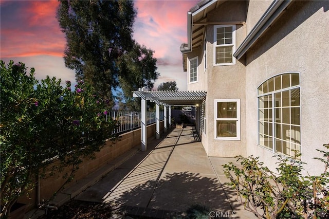 property exterior at dusk featuring a patio, stucco siding, fence private yard, and a pergola