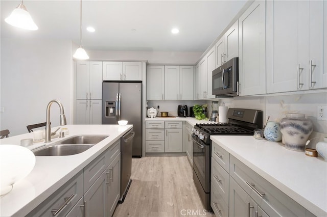 kitchen with gray cabinetry, sink, stainless steel appliances, light hardwood / wood-style flooring, and pendant lighting