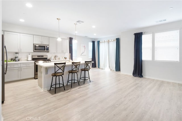 kitchen featuring pendant lighting, a center island with sink, light wood-type flooring, and stainless steel appliances