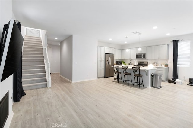 kitchen featuring a kitchen breakfast bar, light hardwood / wood-style flooring, decorative light fixtures, a center island with sink, and appliances with stainless steel finishes