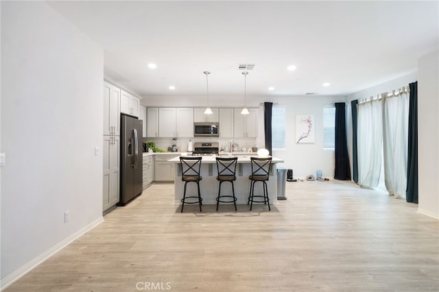 kitchen featuring a kitchen bar, appliances with stainless steel finishes, decorative light fixtures, light hardwood / wood-style flooring, and an island with sink