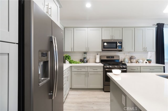 kitchen featuring appliances with stainless steel finishes, tasteful backsplash, light hardwood / wood-style flooring, and gray cabinetry