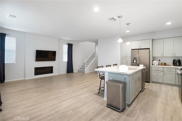 kitchen featuring gray cabinetry, sink, hanging light fixtures, light hardwood / wood-style floors, and a kitchen island with sink