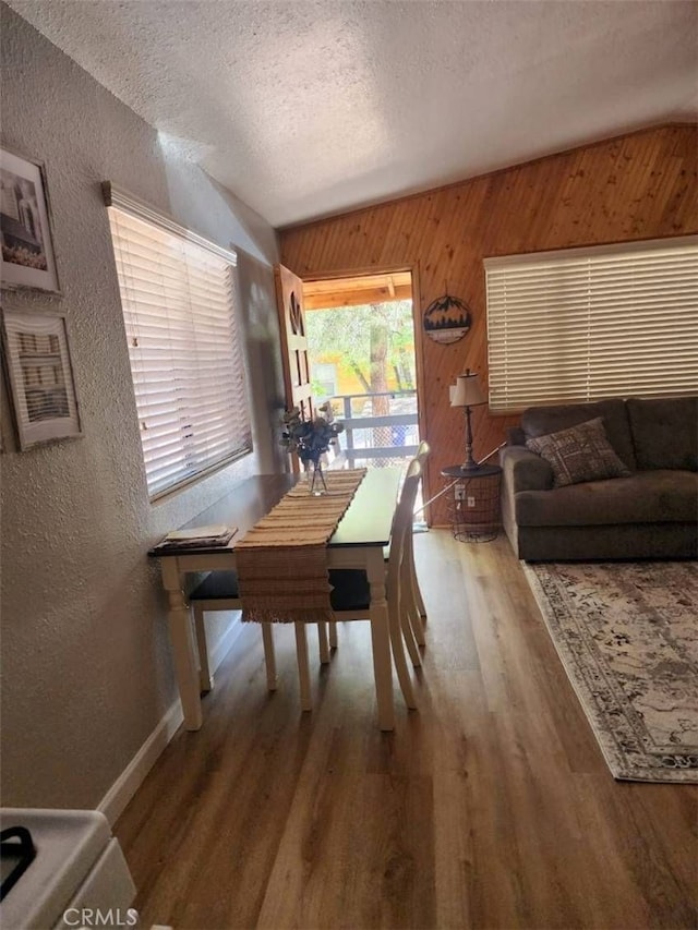 dining area with a textured ceiling, hardwood / wood-style flooring, and wooden walls