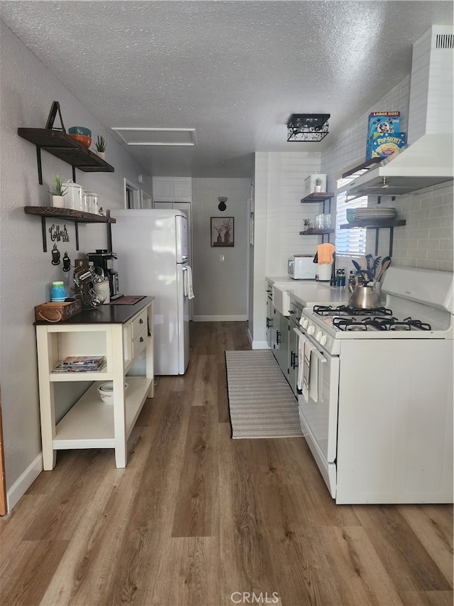 kitchen with wood-type flooring, white appliances, a textured ceiling, and wall chimney range hood