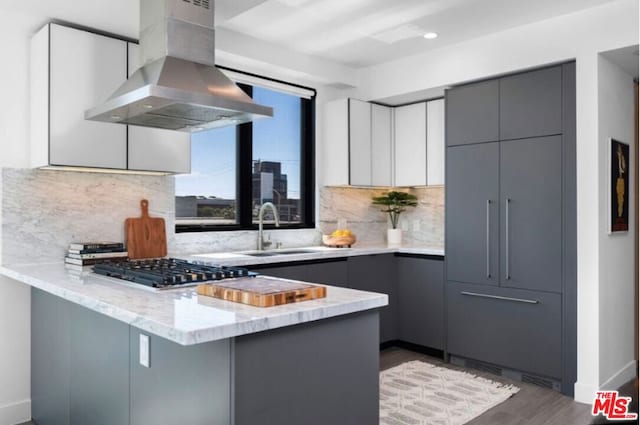 kitchen featuring kitchen peninsula, wall chimney exhaust hood, and gray cabinetry