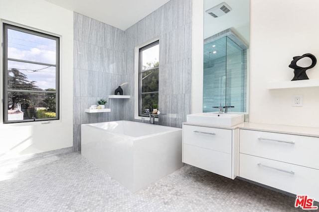 bathroom with tile patterned flooring, vanity, a tub to relax in, and tile walls