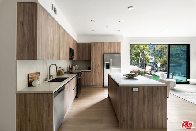 kitchen with a center island, sink, tasteful backsplash, light hardwood / wood-style floors, and stainless steel appliances