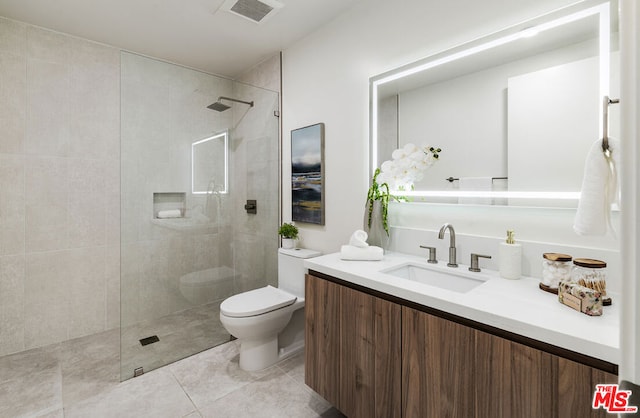 bathroom with tiled shower, vanity, toilet, and tile patterned flooring