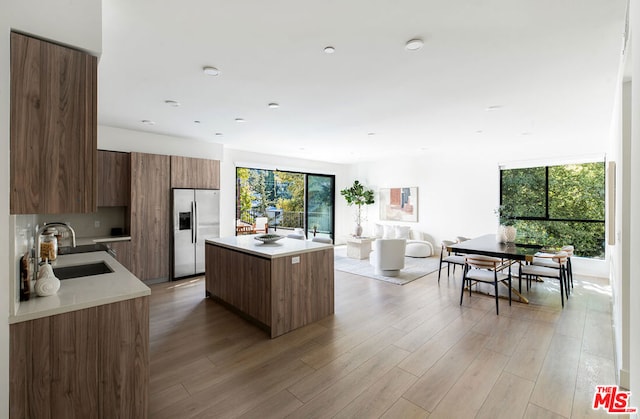 kitchen featuring stainless steel fridge, a kitchen island, light wood-type flooring, and sink