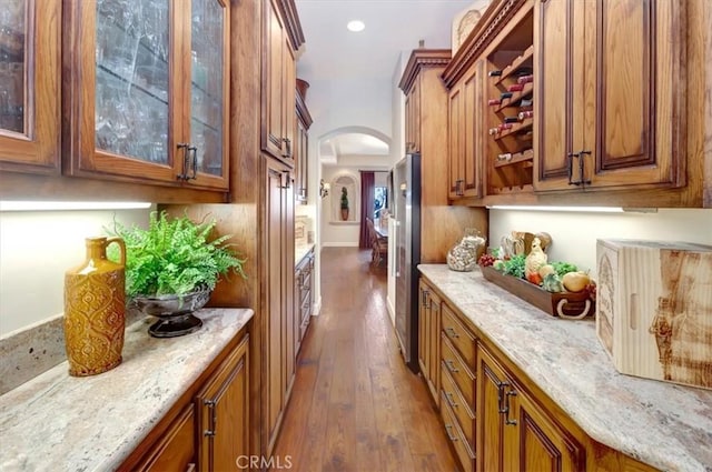 bar featuring stainless steel refrigerator, light stone countertops, and dark hardwood / wood-style floors