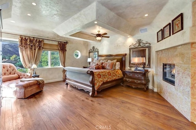 bedroom featuring a tiled fireplace, ceiling fan, and wood-type flooring