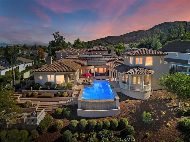 back house at dusk featuring a mountain view and a patio