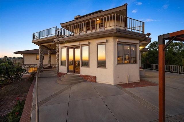 back house at dusk with a balcony and a patio