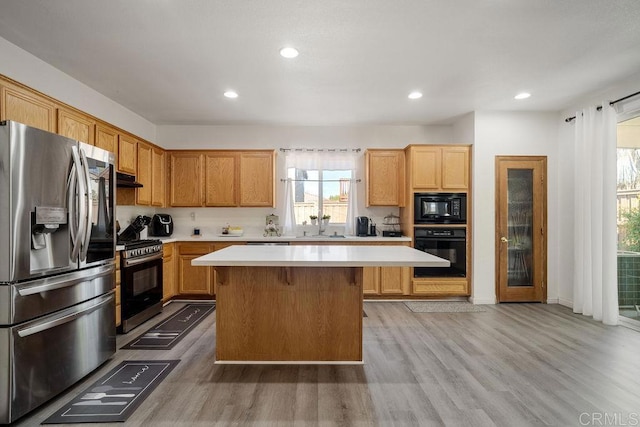 kitchen with light wood-type flooring, a kitchen bar, a center island, and black appliances