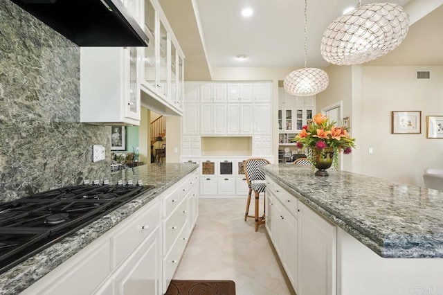 kitchen with decorative backsplash, black gas stovetop, pendant lighting, white cabinets, and a kitchen island