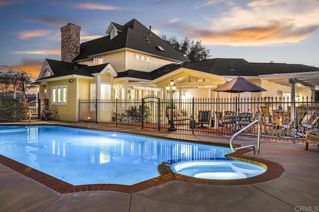 pool at dusk with a patio area and an in ground hot tub