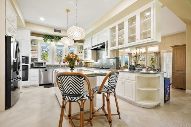 kitchen with white cabinets, light tile patterned floors, range hood, appliances with stainless steel finishes, and decorative light fixtures