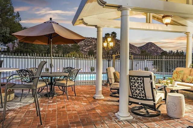 patio terrace at dusk with a mountain view and a fenced in pool