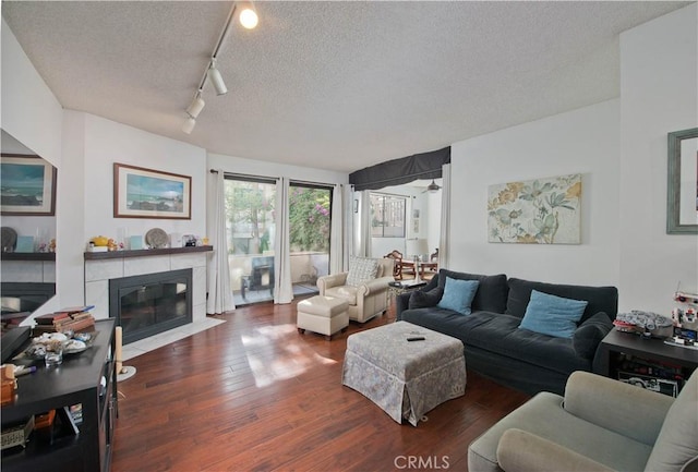 living room with dark hardwood / wood-style flooring, rail lighting, a textured ceiling, ceiling fan, and a fireplace