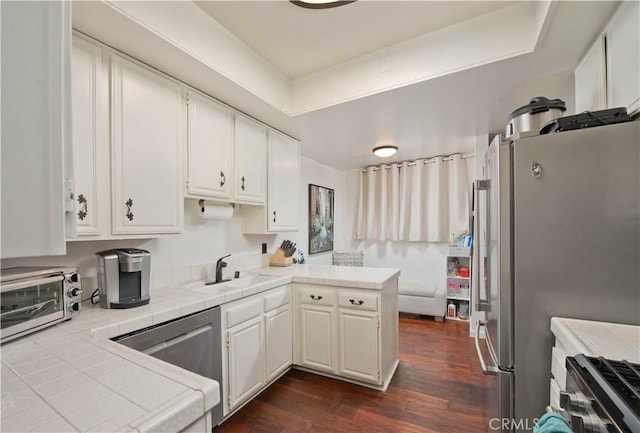 kitchen featuring white cabinetry, tile counters, dark hardwood / wood-style flooring, kitchen peninsula, and appliances with stainless steel finishes