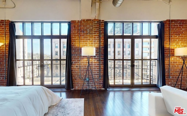 bedroom featuring multiple windows, dark hardwood / wood-style flooring, and brick wall