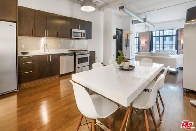 kitchen with dark brown cabinetry, wood-type flooring, a kitchen bar, decorative backsplash, and appliances with stainless steel finishes