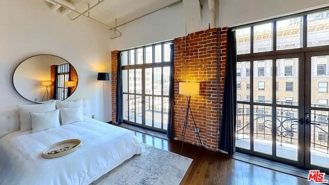 bedroom featuring access to exterior, brick wall, dark hardwood / wood-style flooring, and a high ceiling