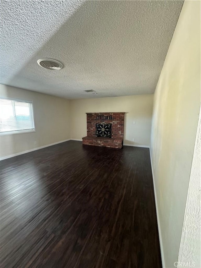 unfurnished living room with a fireplace, a textured ceiling, and dark wood-type flooring