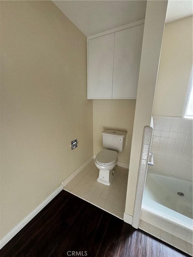 bathroom with a washtub, toilet, and hardwood / wood-style flooring