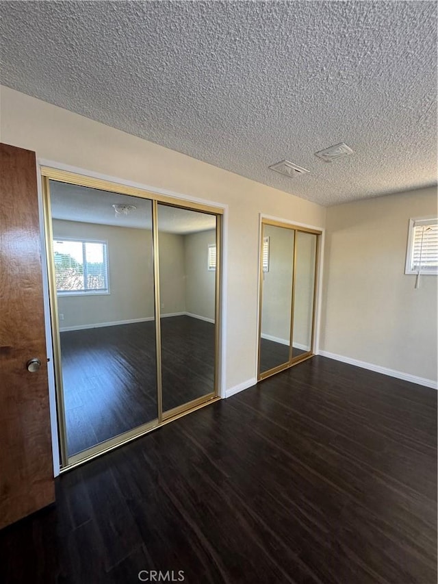 unfurnished bedroom featuring dark hardwood / wood-style flooring, a textured ceiling, and multiple windows