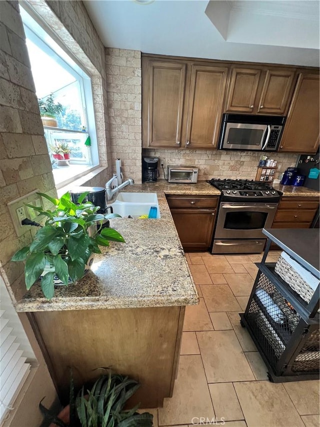 kitchen with tasteful backsplash, appliances with stainless steel finishes, sink, and light stone counters