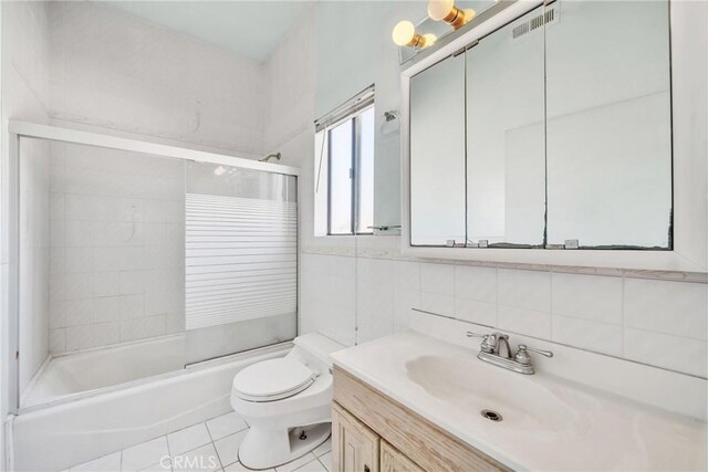 full bathroom with tile patterned flooring, bath / shower combo with glass door, toilet, vanity, and tile walls