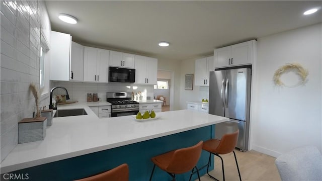 kitchen featuring white cabinets, appliances with stainless steel finishes, sink, kitchen peninsula, and a breakfast bar area