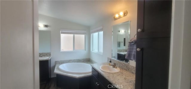 bathroom featuring tiled bath, vanity, and vaulted ceiling