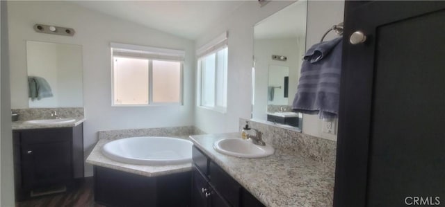 bathroom with tiled bath, vanity, and vaulted ceiling