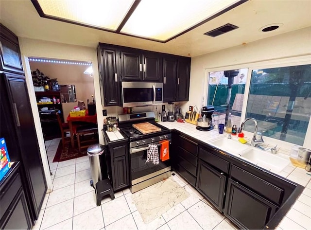 kitchen with tile counters, sink, light tile patterned flooring, and appliances with stainless steel finishes