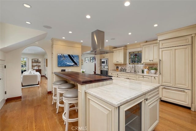 kitchen featuring island exhaust hood, light wood-type flooring, cream cabinetry, a center island, and butcher block countertops