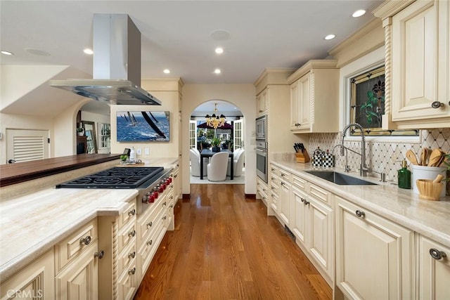 kitchen with island exhaust hood, stainless steel gas cooktop, sink, light hardwood / wood-style flooring, and cream cabinetry