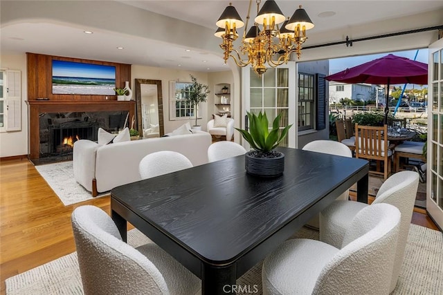 dining space featuring a stone fireplace, light hardwood / wood-style floors, and a notable chandelier